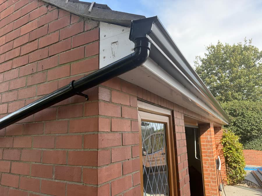 Corner detail of a black seamless gutter with a swan neck downpipe against red brick and white fascia