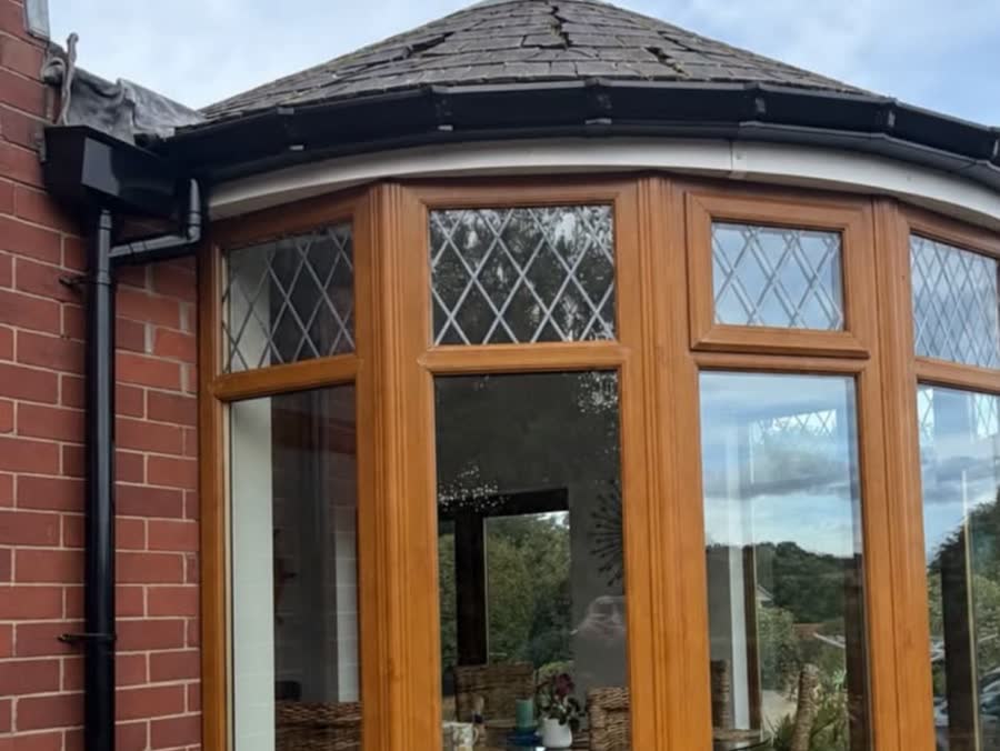 Black seamless gutter curving round a bay window turret with a matching round downpipe