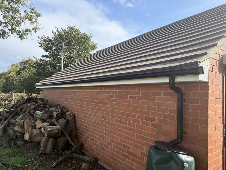 Black seamless gutter and 68mm round downpipe feeding a water butt at a brick outbuilding