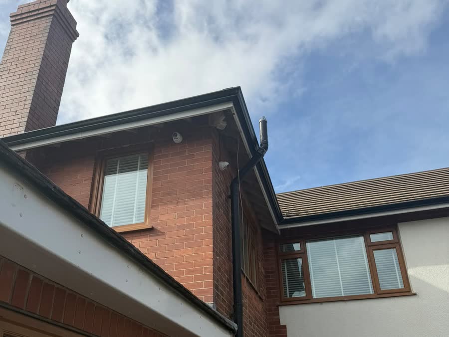 Black seamless guttering over a white fascia with a downpipe running down the corner of a house